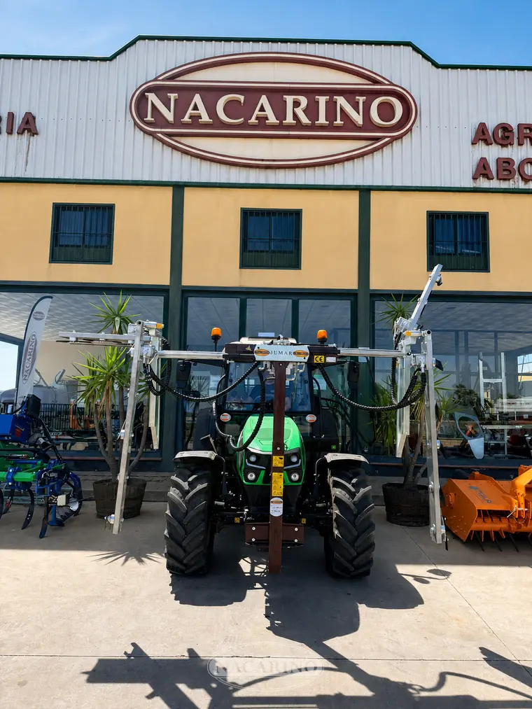 Despuntadora JUMAR de cuchillas montada delante de un tractor verde, con los dos cuerpos de corte abiertos