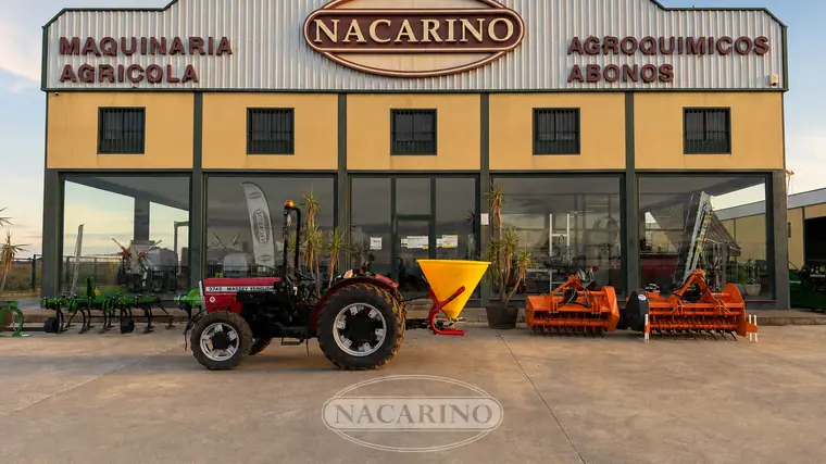 Tractor con abonadora suspendida delante de la nave de Nacarino en Aceuchal