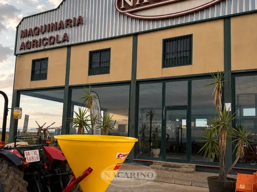 Abonadora de tolva amarilla en tractor delante de la nave de Nacarino en Aceuchal