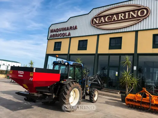 Tractor con abonadora roja delante de la nave de Nacarino en Aceuchal