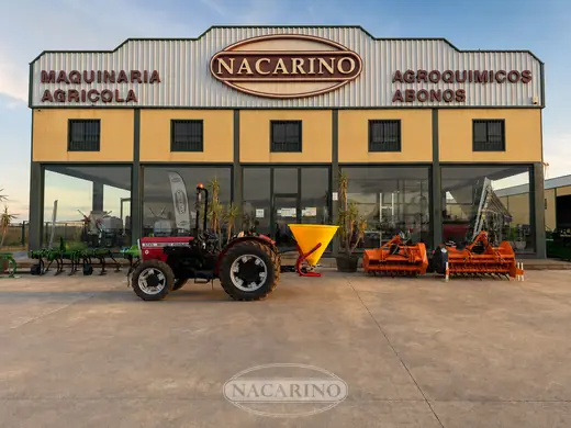Tractor con abonadora de tolva amarilla delante de la nave de Nacarino en Aceuchal