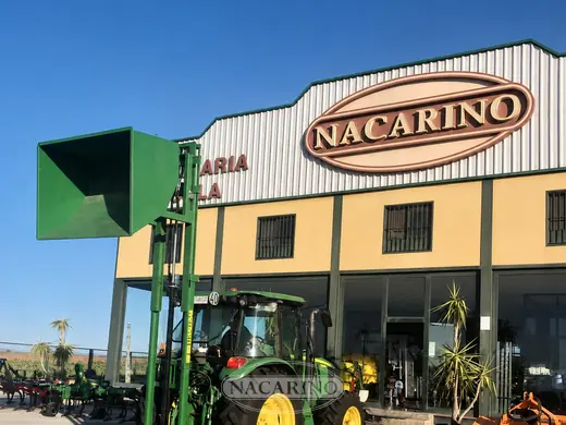 Tractor con tolva elevadora verde delante de la nave de Nacarino en Aceuchal