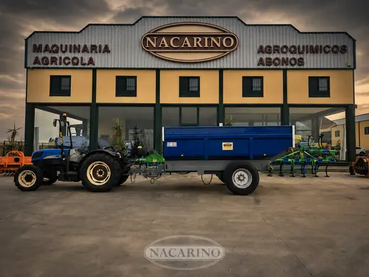 Tractor azul con remolque basculante azul delante de la nave de Nacarino en Aceuchal