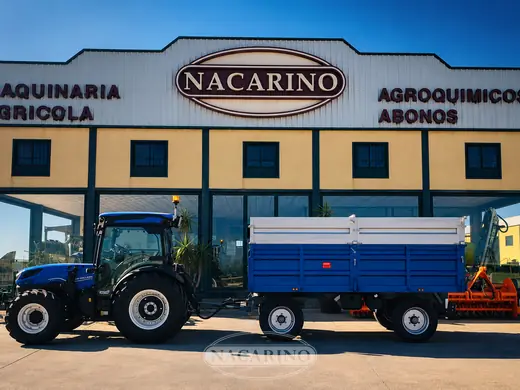Tractor azul con remolque de laterales altos delante de la nave de Nacarino en Aceuchal