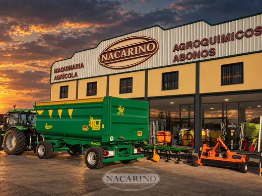 Tractor con remolque agrícola verde delante de la nave de Nacarino al atardecer