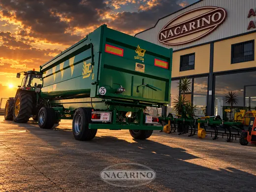 Tractor con remolque verde de laterales altos delante de la nave de Nacarino al atardecer