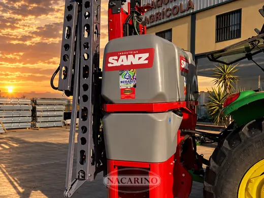 Pulverizador suspendido rojo montado en tractor, delante de la nave de Nacarino