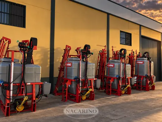 Pulverizadores suspendidos alineados junto a la nave de Nacarino al atardecer